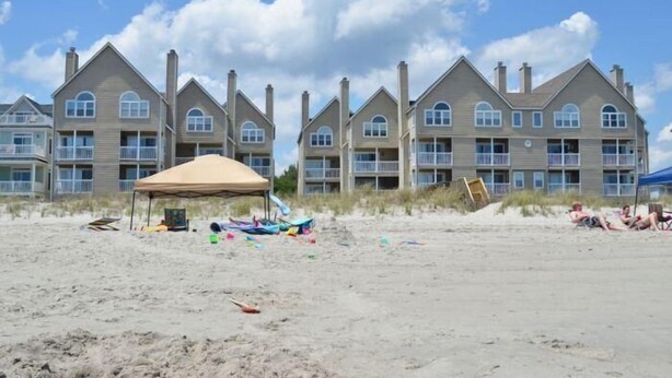 A beachfront hotel with multiple-story buildings, a beach umbrella, and beach chairs. - Cape Coddages I 101 - Oceanfront in Surfside Beach (Surfside Beach)