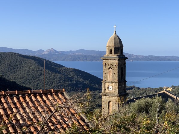 A stone tower with a clock, surrounded by terracotta roof tiles and vegetation.