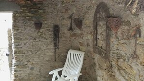 A rustic stone room with a white plastic chair, a red chandelier, and various wall decorations including a heart-shaped item and a metal frame. - At casa di u piratu (FARINOLE)