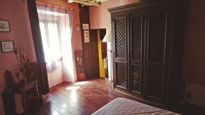 A room with a bed, wooden floor, a wardrobe, a table with a lamp, and a window with curtains. - At casa di u piratu (FARINOLE)