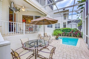 A glass-enclosed patio with a pool, outdoor seating, and a ceiling fan.
