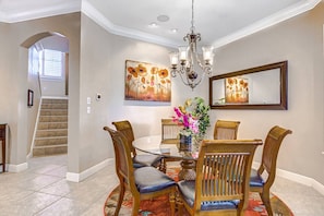 A dining area with a round table, chairs, a chandelier, and artwork on the walls.