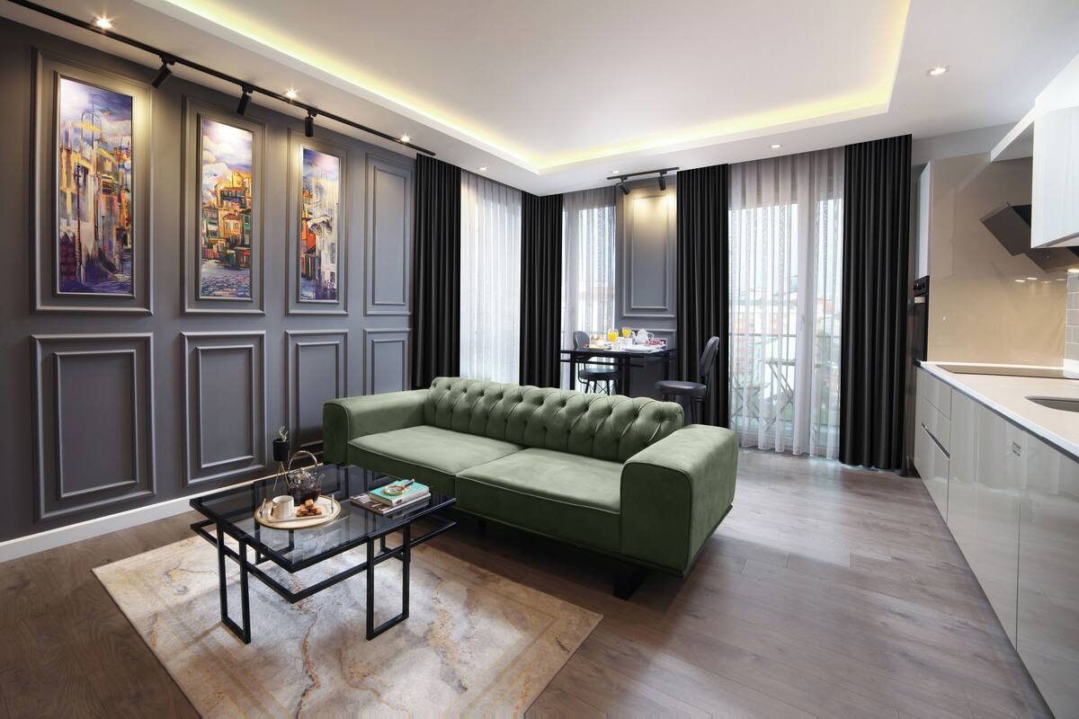 A modern living room with a green sofa, a glass coffee table, and a dining area with a table and chairs.