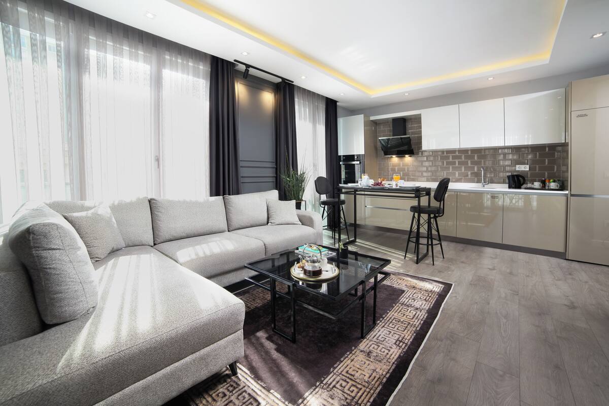 A modern living room with a grey sofa, a glass coffee table, and a dining area with a chair and table.