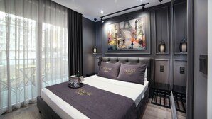 Una habitación de hotel moderna con una cama grande, un cuadro de paisaje urbano en la pared y un balcón con vistas.