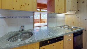 A kitchen with wooden cabinets, a sink, a dishwasher, and a stove. - Very well located apartment house in the favorite and quiet Salet area. (St. Moritz)