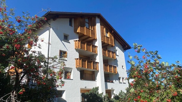 A multi-story building with balconies and windows, surrounded by trees with red berries. - Very well located apartment house in the favorite and quiet Salet area. (St. Moritz)