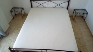 A single bed with a metal frame and a white mattress in a room with plain walls and a carpeted floor. - Ikia apartment Ierissos  (Ierissos)