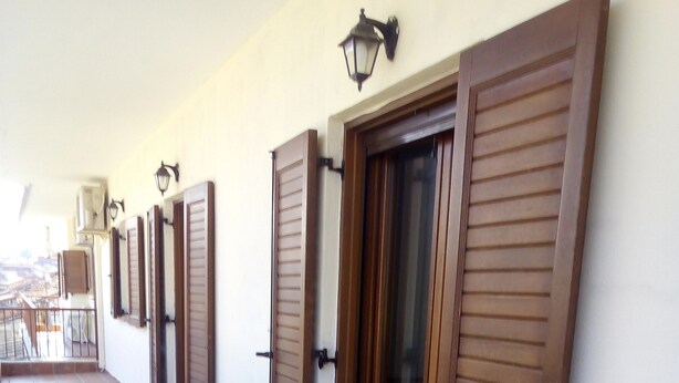 A corridor with tiled flooring, wooden shutters on the walls, and a balcony with outdoor furniture. - Ikia apartment Ierissos  (Ierissos)