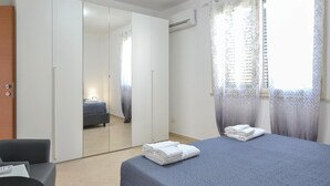 Ein Schlafzimmer mit einem Bett, einem Sessel, einem Kleiderschrank und einem Fenster mit Vorhängen.