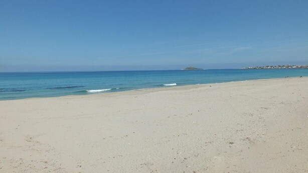 Ein weiter Sandstrand mit ruhigem, blauen Wasser und blauem Himmel.