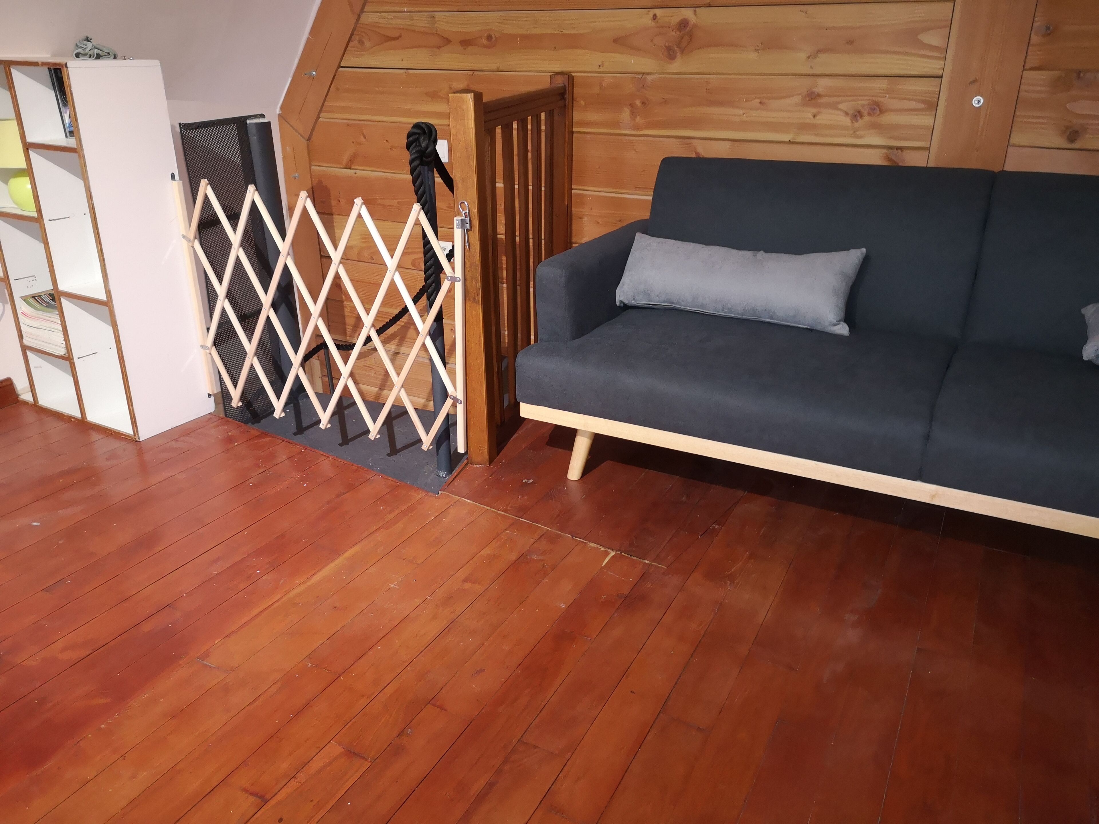 Ein Zimmer mit einem dunkelblauen Sofa, Holzboden, einem weißen Schrank und einer Holzwand mit Seilabsperrung.