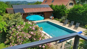 Un área de piscina con vista despejada, una terraza de madera y un edificio con techo de tejas rojas.