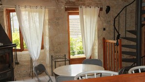 Un interior rústico de piedra con una mesa y sillas de madera, una chimenea y una escalera de caracol.