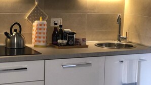 Uma cozinha moderna com armários brancos, uma pia de aço inoxidável e uma chaleira sobre o balcão.