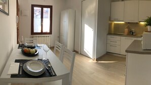 Cozinha compacta com armários brancos, área de jantar com mesa posta para dois e janela que oferece luz natural.