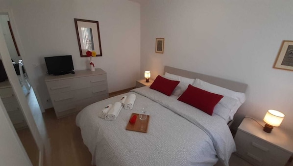 Una habitación de hotel con cama, mesitas de noche, televisor y espejo.