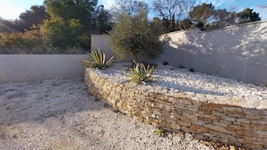 Un jardín ajardinado con muro de piedra, suelo de grava y diversas plantas.