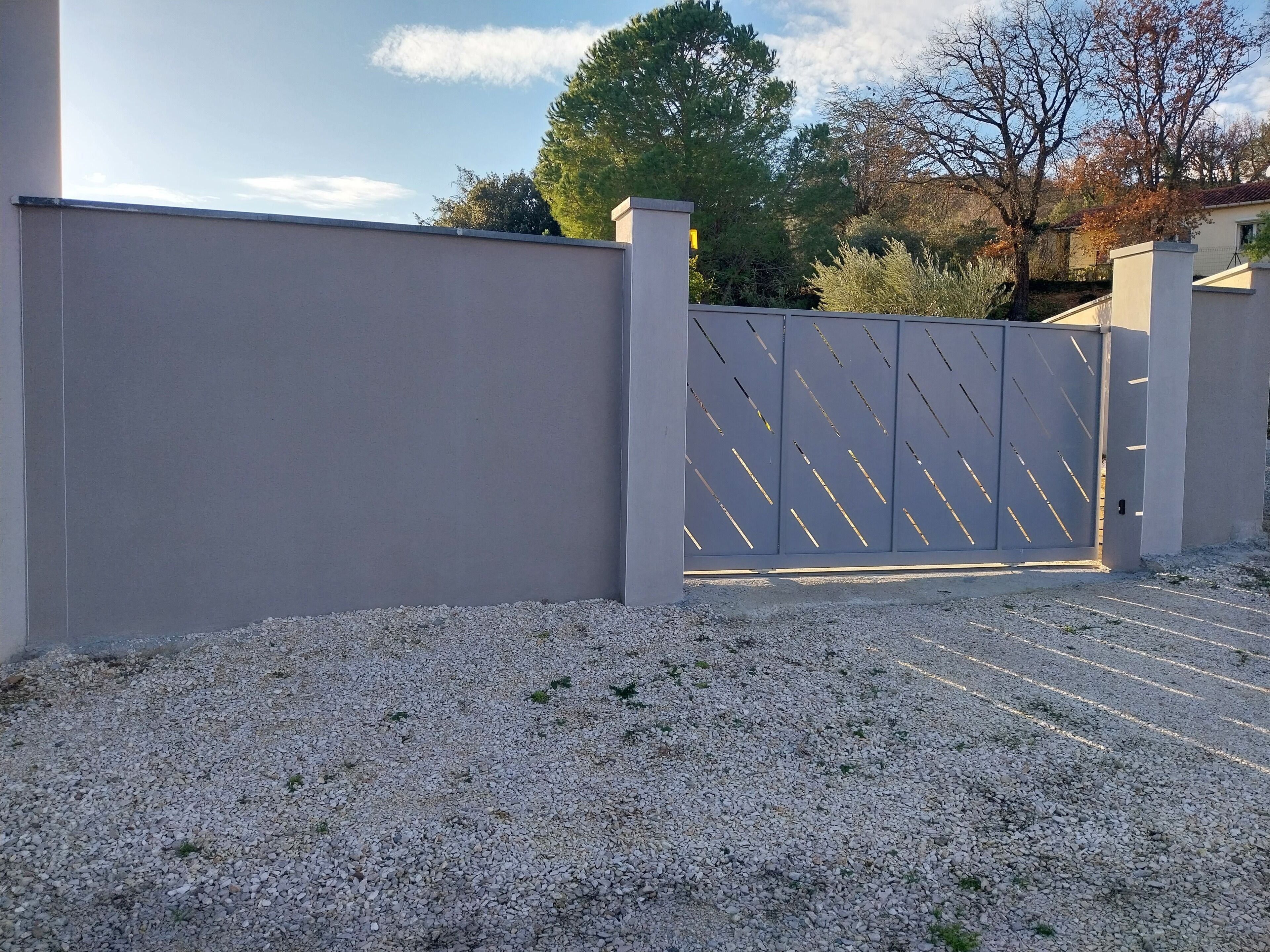 Une allée privée, fermée par un portail, dont la surface est recouverte de gravier et qui mène à un bâtiment.
