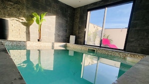 Una piscina interior con agua cristalina, rodeada de paredes de piedra oscura y un ventanal grande.