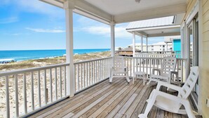 A wooden deck with white railings overlooking a beach.