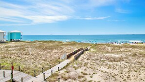 A beach view with a wooden boardwalk leading to a building, a sandy beach, and the ocean.