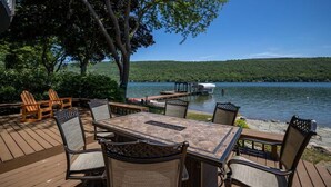 Terraza exterior con una mesa y sillas, con vista a un lago con muelle y embarcación.