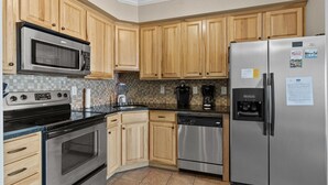 A modern kitchen with wooden cabinets, stainless steel appliances, and a tiled backsplash.