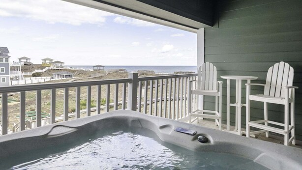 A hot tub on a balcony with a view of the beach and houses.