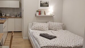 Una camera compatta con un letto, comodino e un angolo cottura.