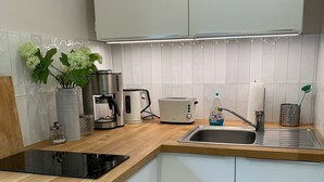 Una cucina moderna con mobili bianchi, un piano di lavoro in legno, un piano cottura integrato, una macchina da caffè, un tostapane e un lavandino.