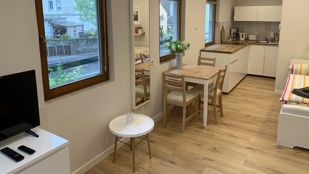Una cucina compatta con zona pranzo, un piccolo tavolo bianco e un televisore su un mobiletto.