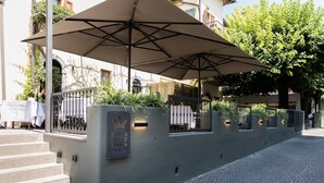 Entrada de hotel con un área de estar al aire libre techada, escalones que conducen a la entrada y un camino pavimentado.
