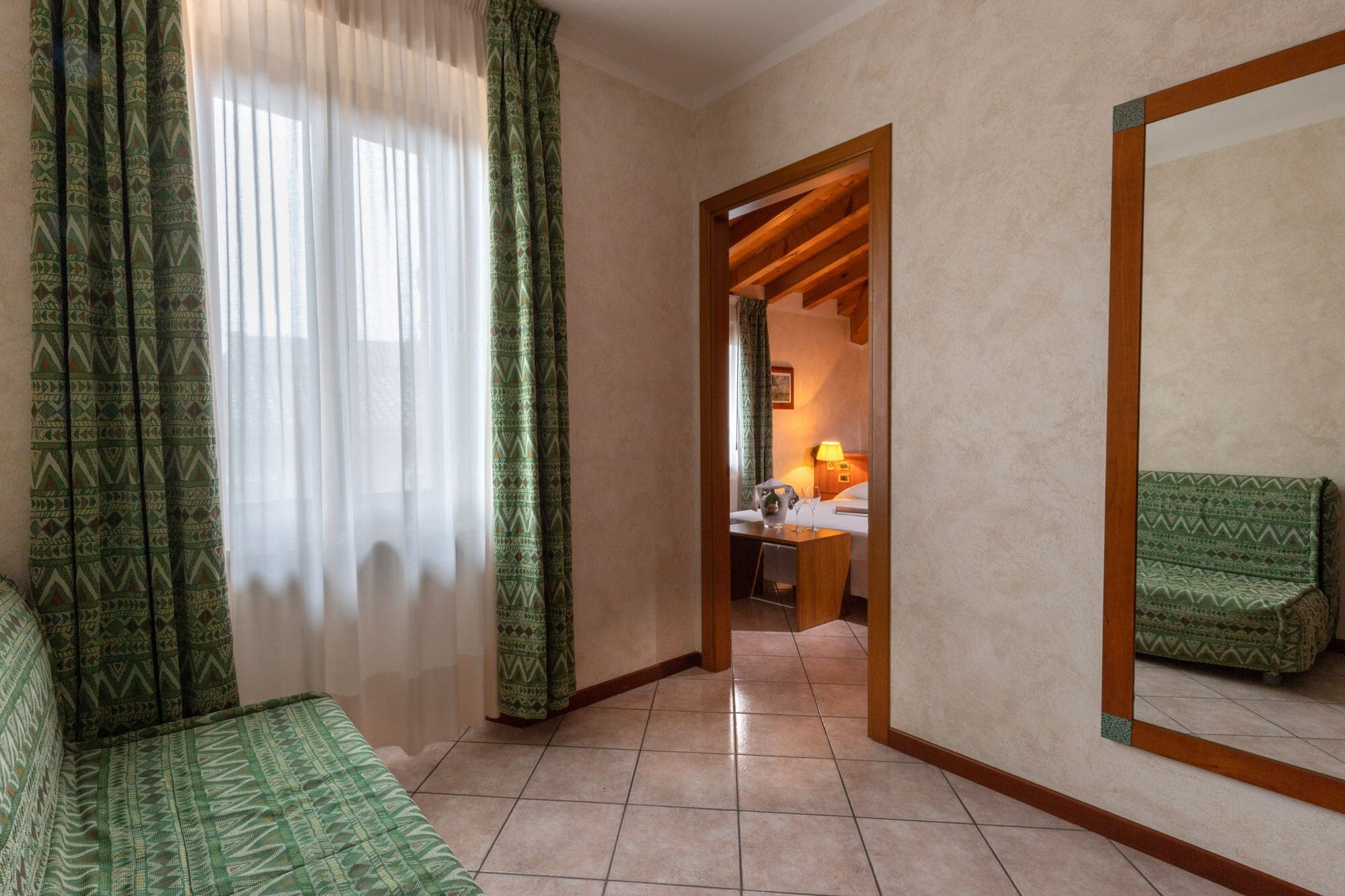 A hotel room with a bed, a bedside table, a lamp, and a green patterned sofa.