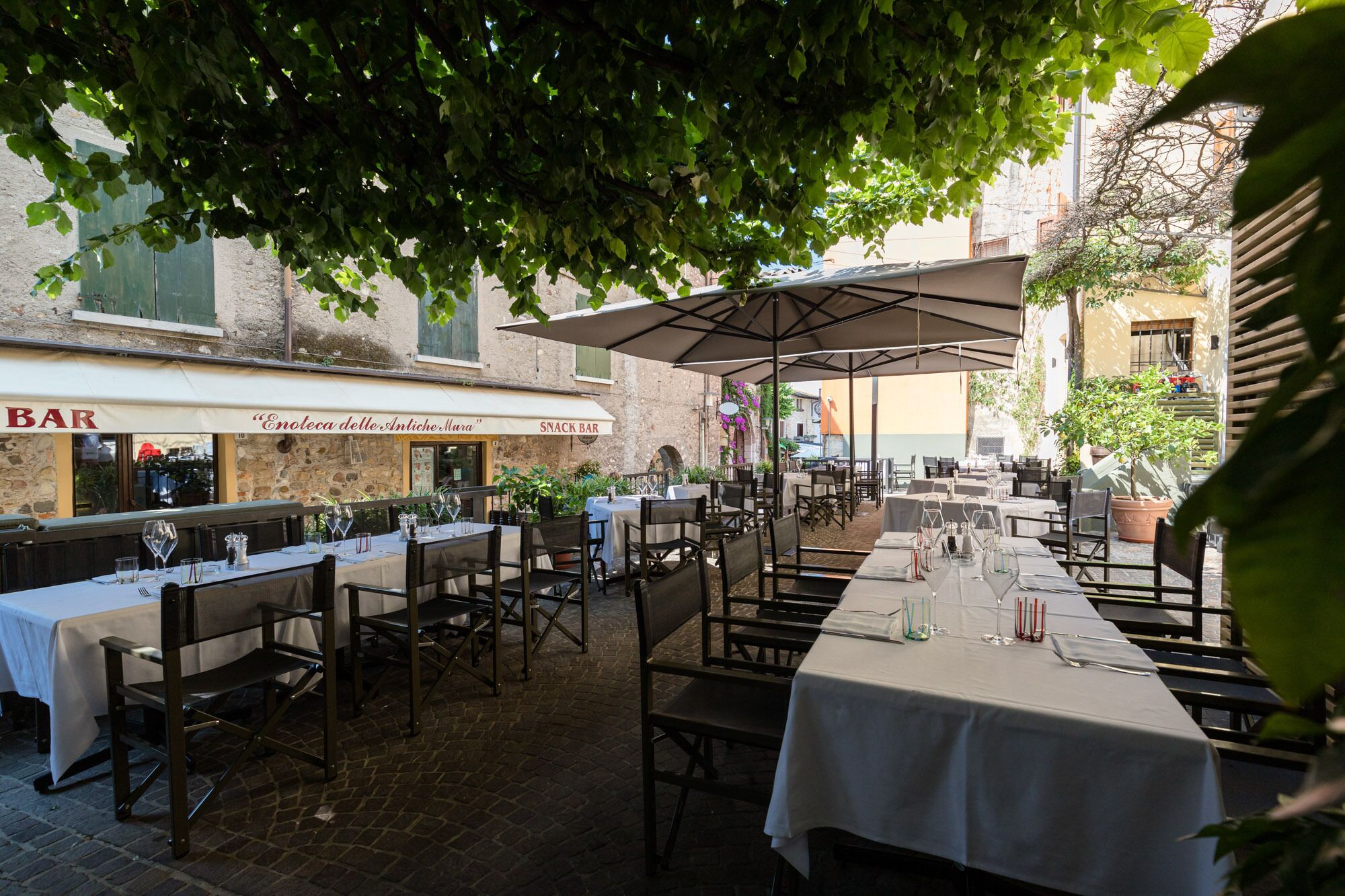 Un área de comedor al aire libre con mesas y sillas, un espacio de estar techado y un bar al fondo.