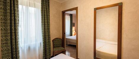 A hotel room with a bed, a chair, a large mirror, and patterned curtains.