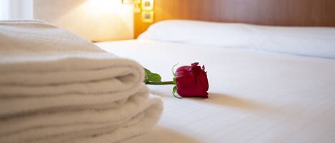 A neatly made bed with a single red rose and a stack of white towels.