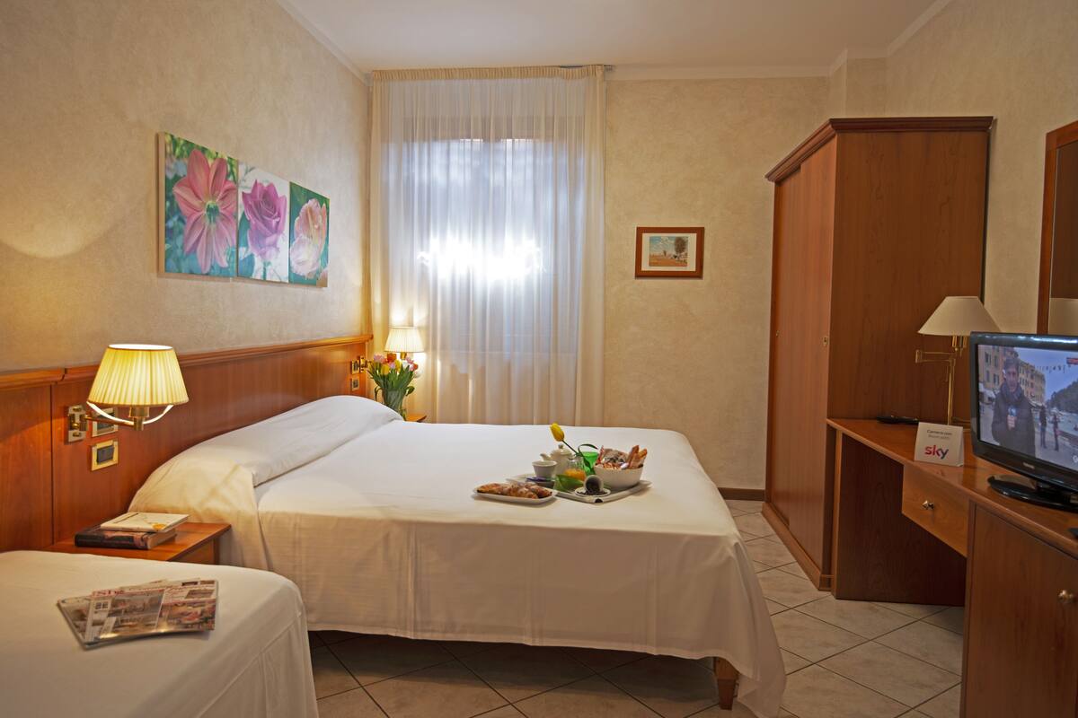 A hotel room with two beds, a television, a desk with a lamp, and a painting on the wall.