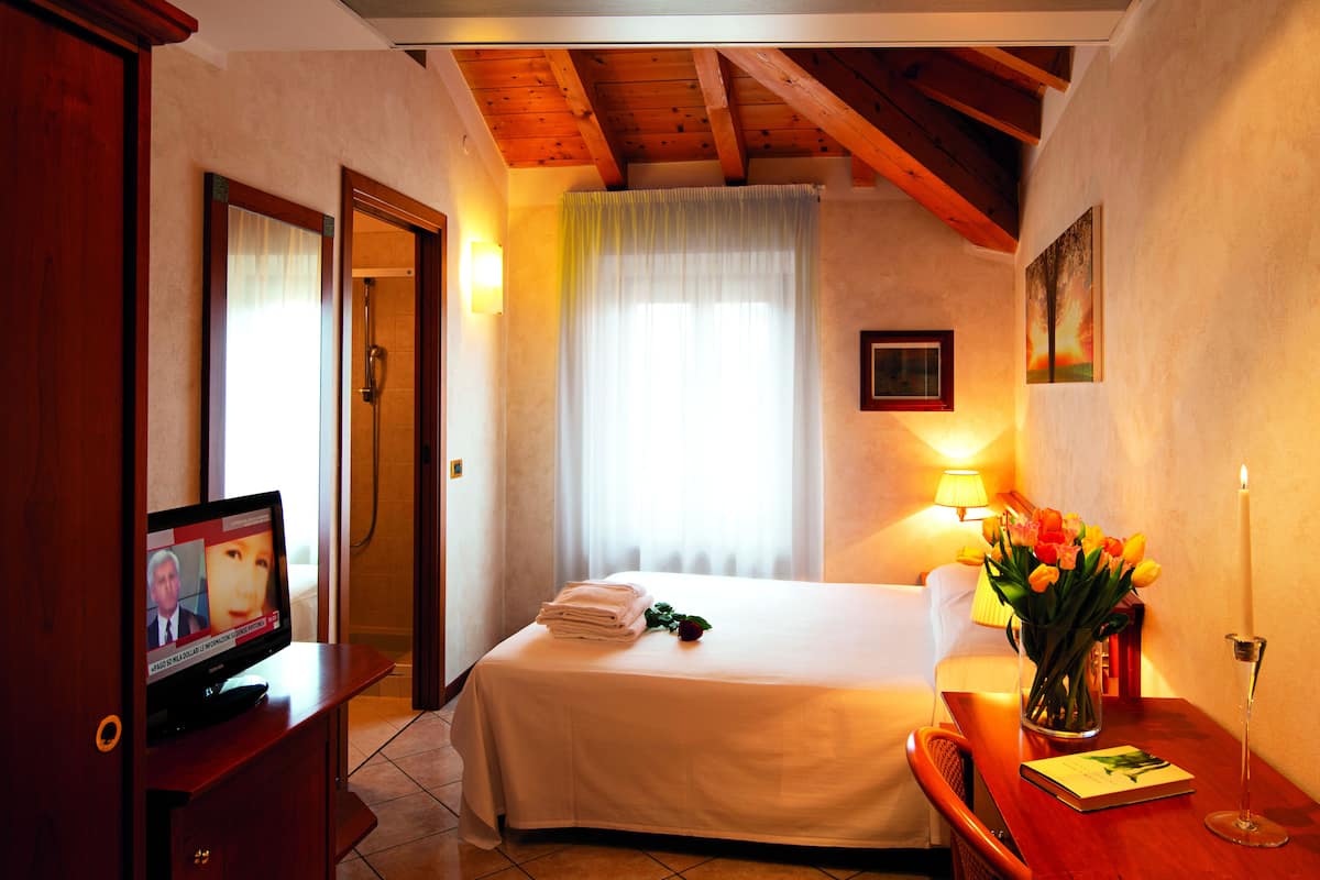 A hotel room with a bed, a desk with a lamp, a TV, and a window with curtains.