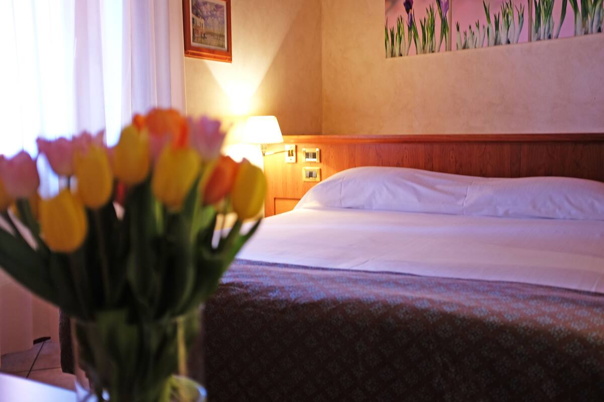 A hotel room with a bed, a nightstand, a lamp, and a wall painting.