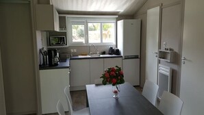 Une cuisine compacte avec des meubles blancs, une table à manger avec des chaises et une fenêtre qui laisse entrer la lumière naturelle.