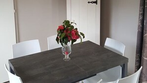 Un coin repas avec une table en bois foncé, des chaises blanches et un vase rempli de fleurs.