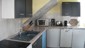 A compact kitchen with a sink, stove, microwave, coffee maker, kettle, and dishwasher.