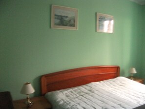 A bedroom with a wooden headboard, a bed with a white quilt, two bedside lamps, and two framed pictures on the wall.