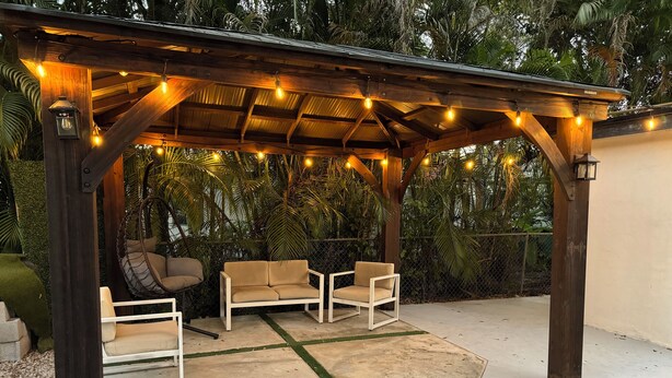 Un patio exterior con una pérgola de madera, luces colgantes y dos sofás color beige.