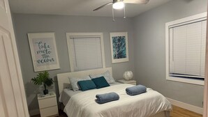 Un dormitorio con una cama, dos mesitas de noche, un ventilador de techo y una ventana con persianas.