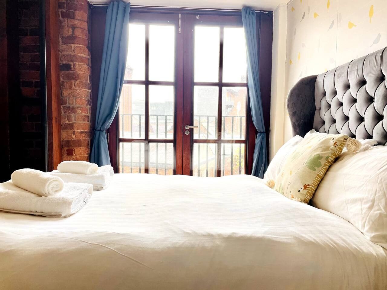 Habitación de hotel con una cama grande, vista a través de un ventanal y una pared de ladrillo.