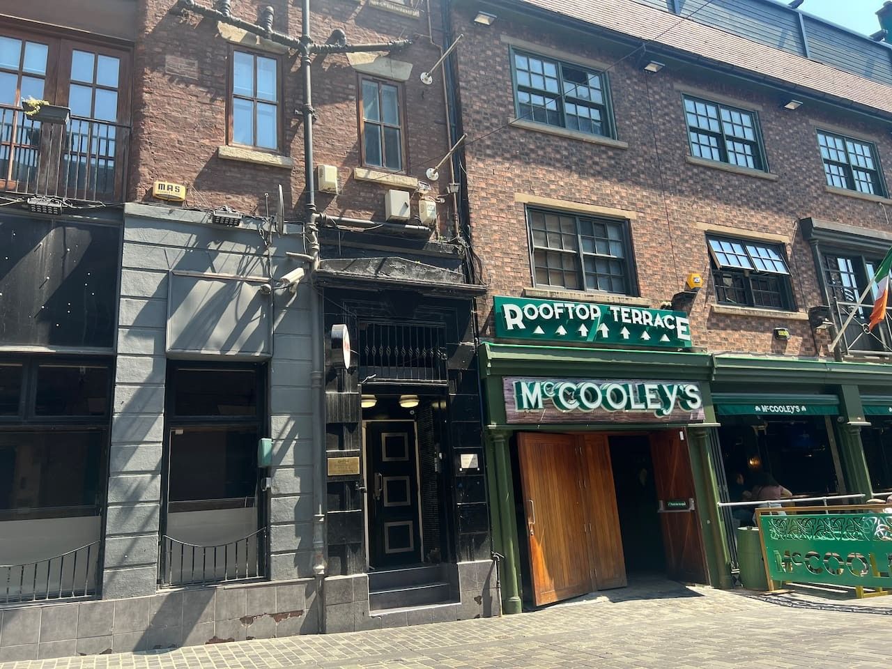 A building with a green awning labeled 'McCool's' and a sign for 'Rooftop Terrace.'