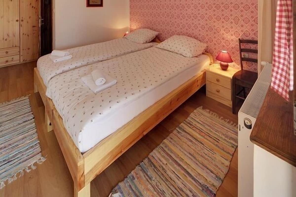 Une chambre à coucher avec un lit en bois, une table de chevet, une lampe, un mur à motifs et une porte donnant sur une salle de bain.