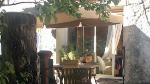 Ein Terrassenbereich im Freien mit einem Holztisch, Blumentöpfen und einem großen Baumstamm.